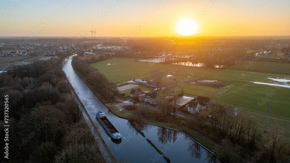 This aerial photograph captures the serene essence of dawn, with the early sunlight gently breaking over a quiet, meandering canal. A lone boat is moored alongside, still in the calm of the morning
