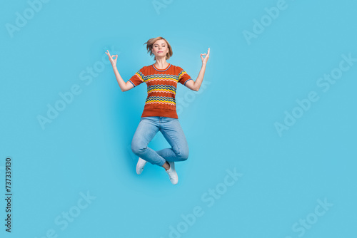 Full length photo of charming focused girl wear strited t-shirt jeans levitating in meditation asana isolated on blue color background