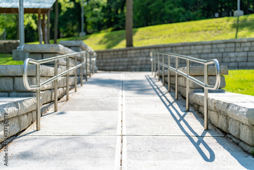 Outdoor, exterior gray concrete ramped sidewalk with stainless steel railings. 