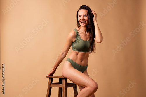 Photo of stunning cheerful girl wear stylish top and panties sit stool advertise activewear isolated on beige color background