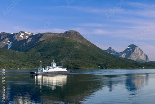 A ferry journey across a glassy fjord, bordered by verdant slopes and towering peaks under a clear blue sky, captures the essence of Nordic serenity