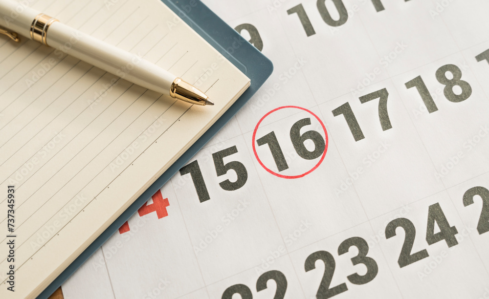notebook and pen on a calendar highlighting the 16th marked with a red circle on the calendar notebook and pen on a calendar highlighting the 16th marked with a red circle on the calendar