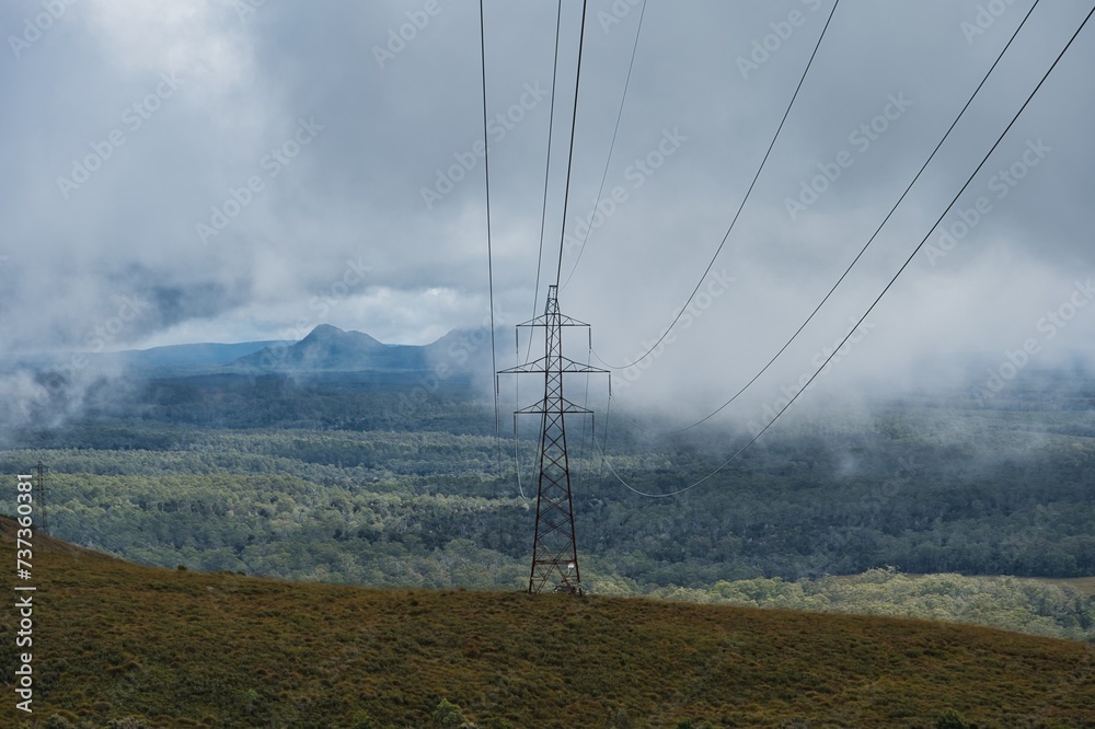 High voltage power lines in front of a cloudy mountain and forest ...