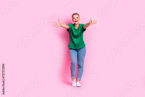 Full size photo of cheeful friendly girl dressed green t-shirt jeans stretching arms to embrace you isolated on pink color background photo