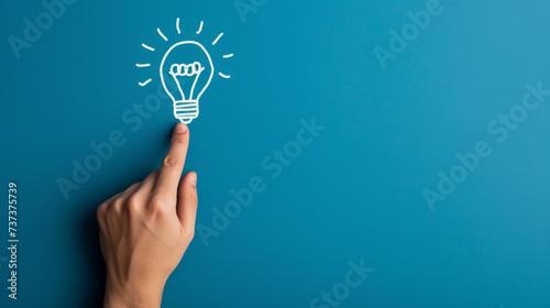 A hand touching a drawn lightbulb symbolizing an idea on a teal background.