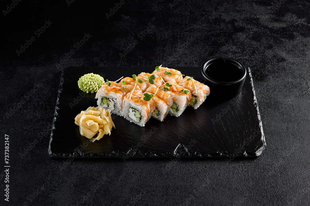 Shrimp roll with shrimp on top and cucumber and cheese inside, on a black slate with soy sauce, wasabi, and ginger Shrimp roll with shrimp on top and cucumber and cheese inside, on a black slate with soy sauce, wasabi, and ginger