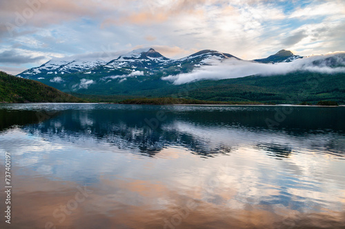 Irradiated water in the sea in a fjord in Norway. Snowy high mountains in the clouds at sunset. © Jan