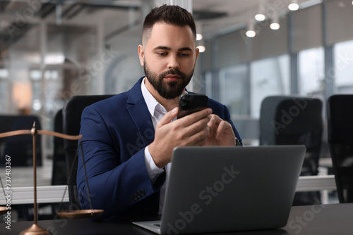 Serious lawyer with smartphone near laptop at table in office