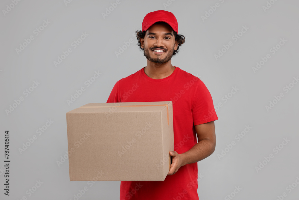Happy young courier with parcel on grey background Happy young courier with parcel on grey background