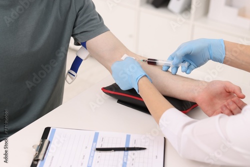 Doctor taking blood sample from patient with syringe at white table in hospital, closeup photo