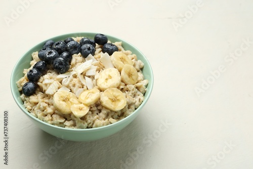 Tasty oatmeal with banana, blueberries, coconut flakes and honey served in bowl on beige table, space for text