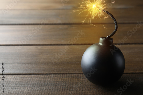 Old fashioned black bomb with lit fuse on wooden table, space for text photo