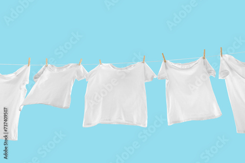 T-shirts drying on washing line against light blue background, low angle view