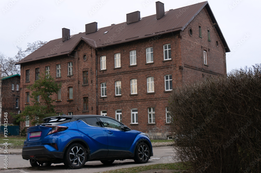 Modern car against the background of old large brick house (called “familok” in Silesia). Dabrowa Gornicza, Poland.