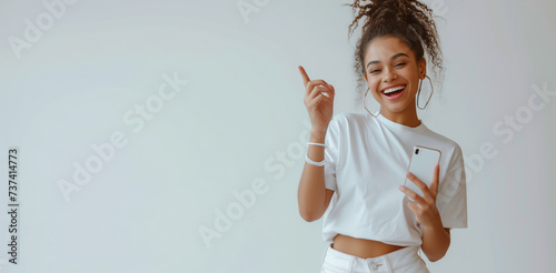 Happy young woman with phone pointing up on white background