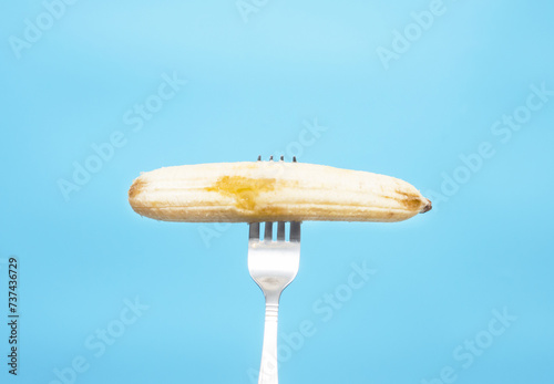 Banana on a fork on a blue background. Copy space. Ripe delicious banana pricked on a kitchen fork photo