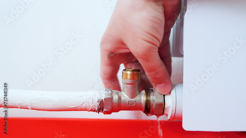 Plumber untightened the valve at the heater. Worker hands repairing radiator. Removing air from the radiator and fixing a heating problem. photo