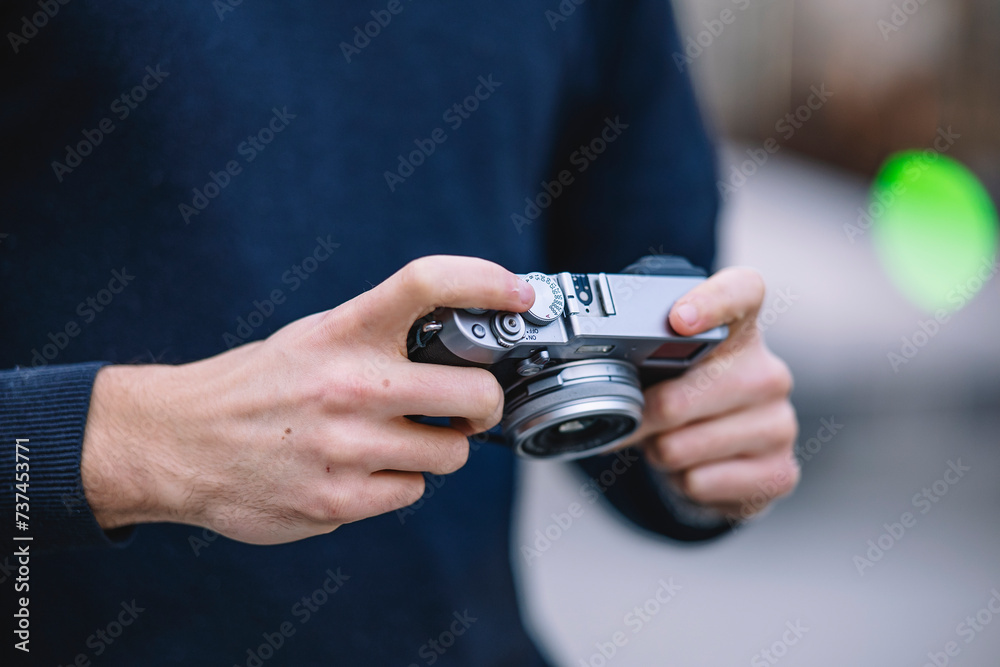 Close-up of a man's hands adjusting the settings on a vintage camera with a blurred urban background