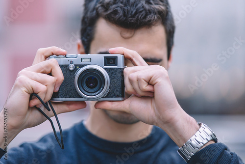 Young man capturing a moment with a vintage camera, focus on camera with blurred background photo
