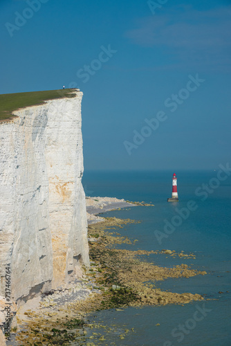 Lighthouse at the end of white walls topped with grass rising above blue sea