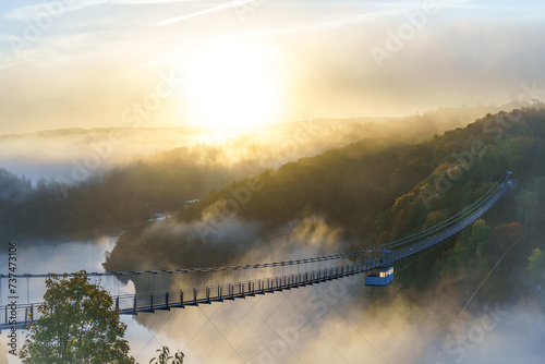 Blick zur Hängebrücke Titan RT an der Rappbodetalsperre im Harz. Die Sonne scheint über die Wipfel und taucht die nebelverhangene Landschaft über dem Bodetal in ein goldenes Licht. photo