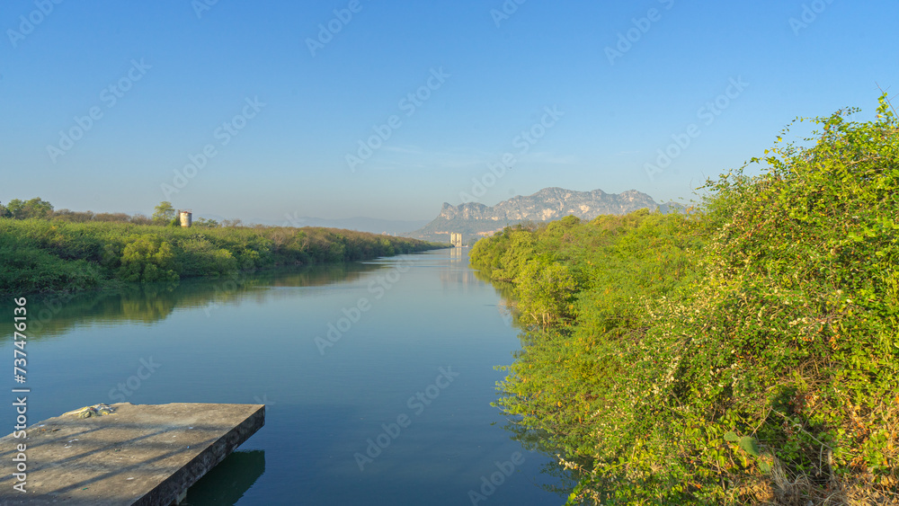 Image of natural scenery in the morning There is a clear, turquoise water source. Reflecting among the green leaves, it looks beautiful. The scenery in the background is a long limestone mountain. 