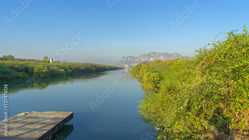 Image of natural scenery in the morning There is a clear, turquoise water source. Reflecting among the green leaves, it looks beautiful. The scenery in the background is a long limestone mountain. 