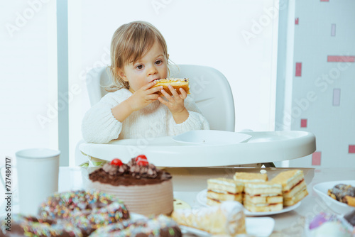 Cute toddler eats cake with chocolate, harm from sugar to the health of a child, tooth problems, dentist for kid. Messy eating of sweets. When it is time to star giving child sugar.