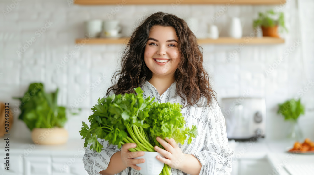 fat overweight smiling young woman with a bunch of greens on the background of a white kitchen, proper nutrition, salad, celery, weight loss, lifestyle, health, girl, food, cooking