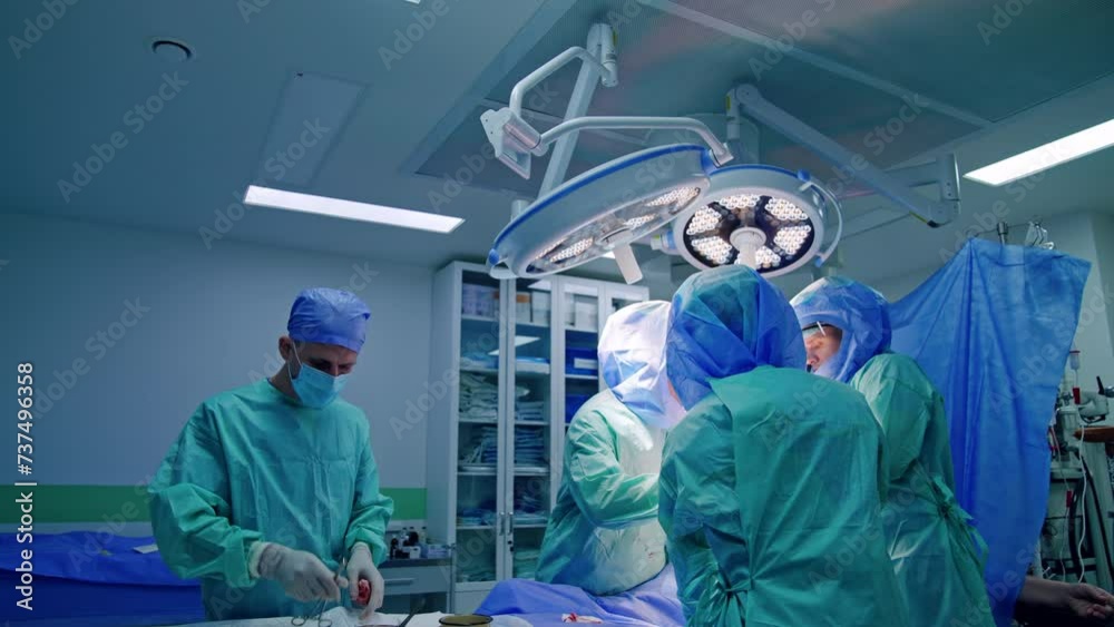 Male assistant arranges the tools on the surgical stand. Team of doctors in protective helmets work at operational table. Male assistant arranges the tools on the surgical stand. Team of doctors in protective helmets work at operational table.