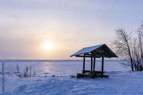 Winter landscape with an empty wooden gazebo on snow covered beach