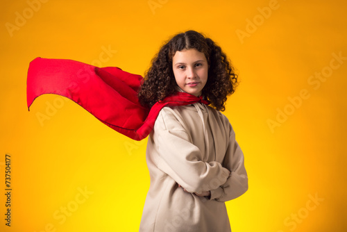 Girl superhero in a red cloak on yellow background. Concept of victory and success. © Aleksej