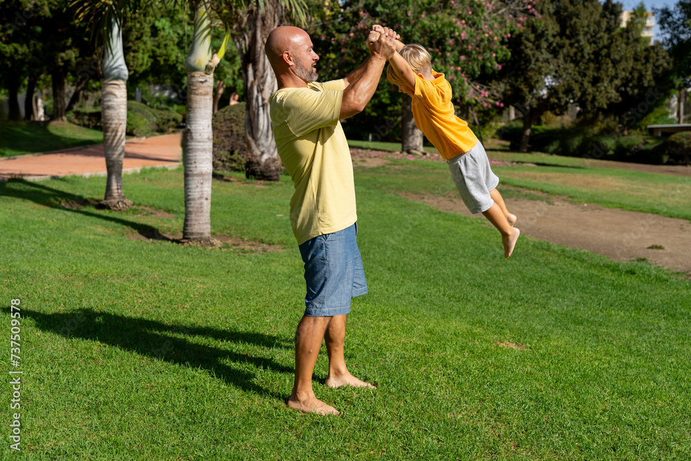 A happy father throws his son into the air in nature. The kid laughs merrily. A father walks with his son in the park.