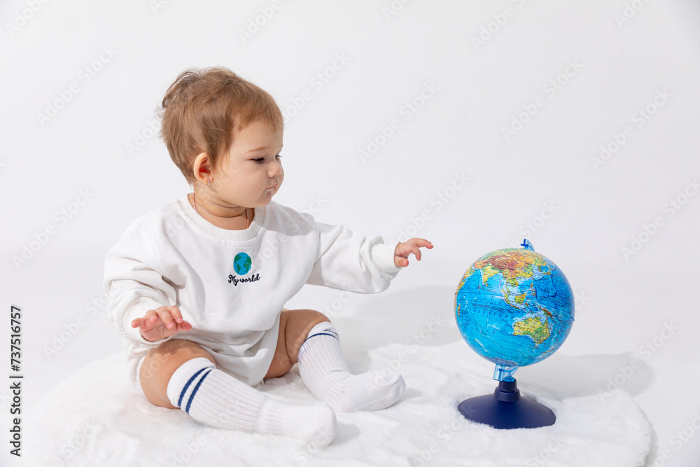 Earth day concept. Portrait of a cute little newborn baby girl in a white bodysuit with inscription my world sitting with the earth globe on white background. Save the planet, kid early education Earth day concept. Portrait of a cute little newborn baby girl in a white bodysuit with inscription my world sitting with the earth globe on white background. Save the planet, kid early education