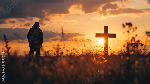 Silhouette of an individual standing before a cross in a field at sunset, evoking a sense of reflection and spirituality.