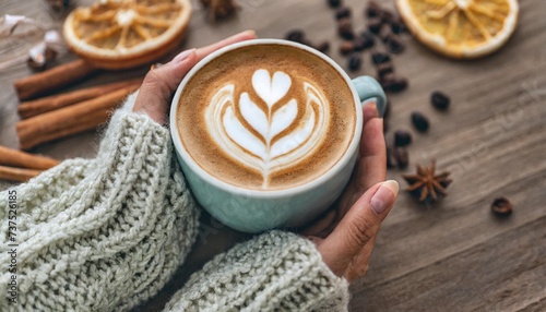 close up of woman in a cosy warm sweater holding a cup of coffee with latte art flat lay with copy space