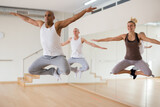 Positive Hispanic man jumping while dancing synchronous group choreography in modern dance studio