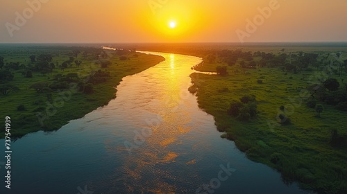 the sun is setting over a river in the middle of a grassy area with trees on both sides of the river.