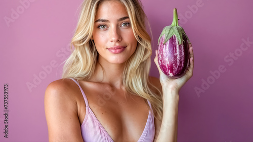 une femme tient une aubergine à côté de son visage avec un petit sourire évocateur