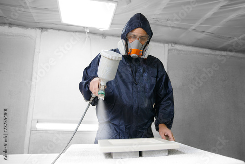 Application white color on facade kitchen furniture, spraying device. Painter staining wood with spray gun