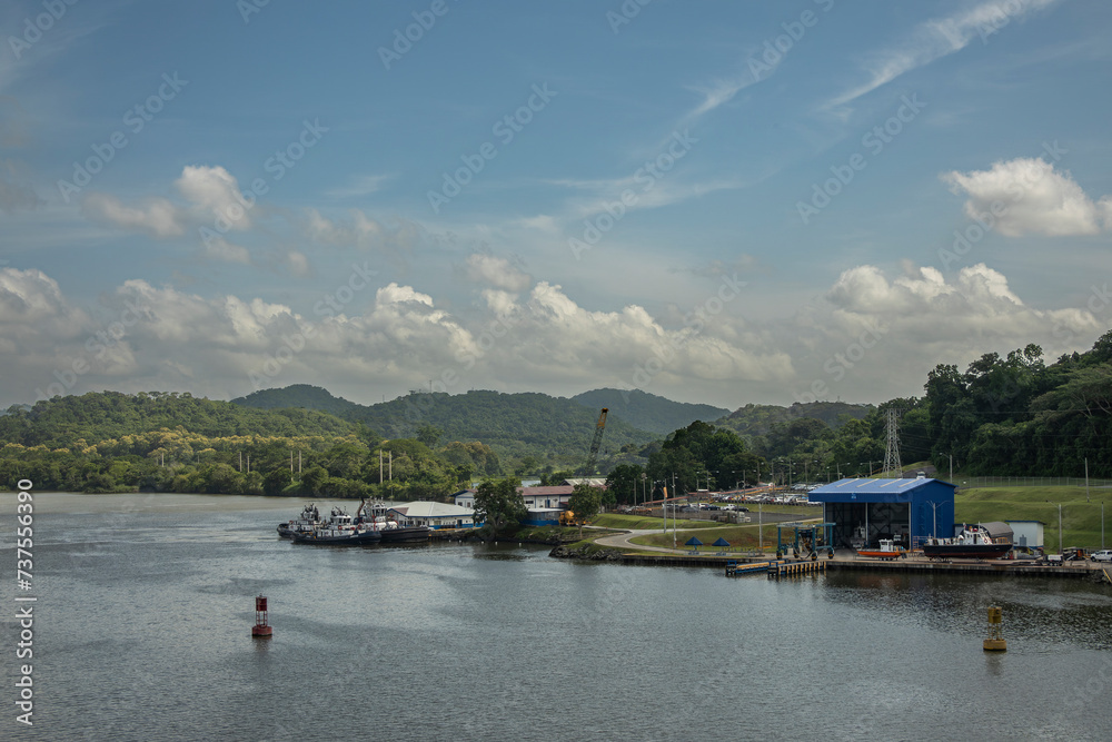 Panama Canal, Panama - July 24, 2023: Just northeast from Miraflores locks landscape. Boat repair shops and ACP Edificio 39 quays. Landscape, forested hills under blue cloudscape
