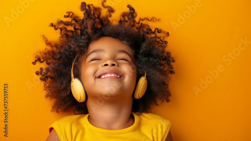 Happy smiling child enjoys listens to music in headphones over orange background photo