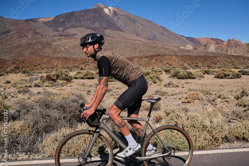 Man cyclist pedaling on road with view on mountain Teide volcano,Tenerife,Canary Islands,Spain. Sportsman training hard on bicycle outdoors.Sport motivation.Cycling training outdoors.Hipster cyclist.