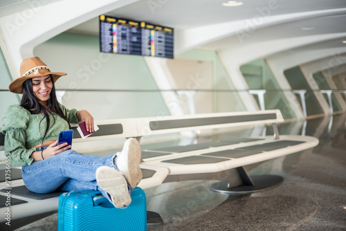 latin girl waiting at the airport texting with smartphone