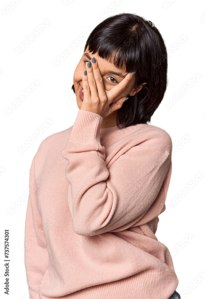 Young Hispanic woman with short black hair in studio blink at the camera through fingers, embarrassed covering face. Young Hispanic woman with short black hair in studio blink at the camera through fingers, embarrassed covering face.