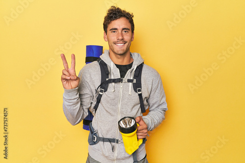 Hiker with backpack and lantern on yellow showing number two with fingers.