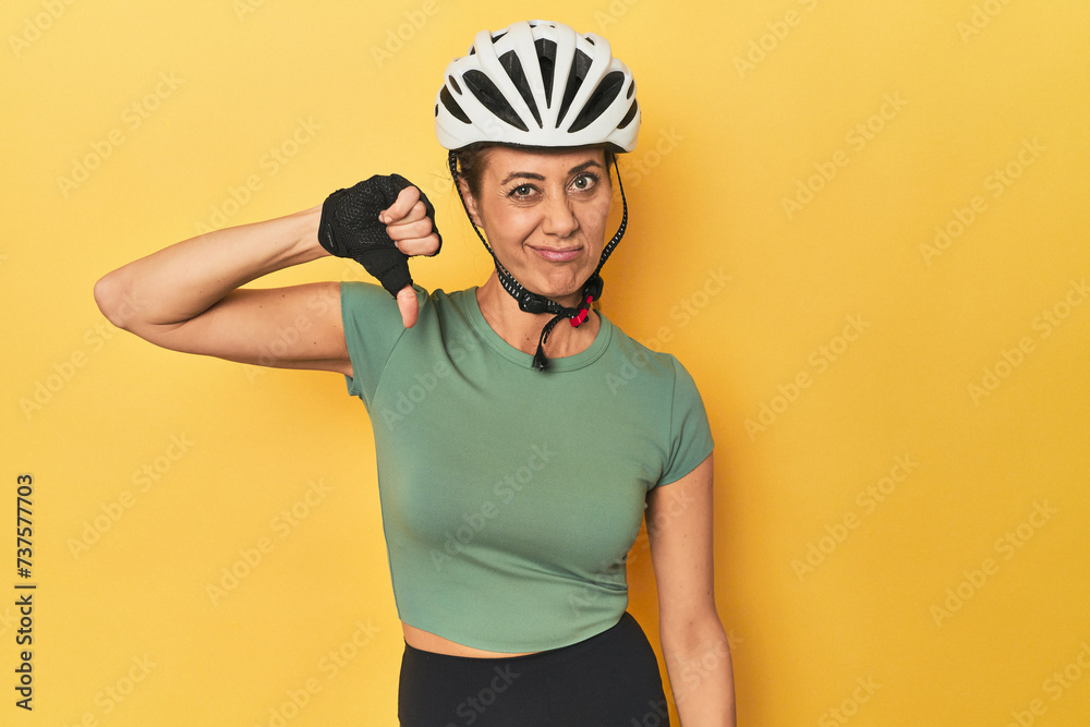 Cyclist middle aged woman with helmet and gloves posed showing a dislike gesture, thumbs down. Disagreement concept. Cyclist middle aged woman with helmet and gloves posed showing a dislike gesture, thumbs down. Disagreement concept.