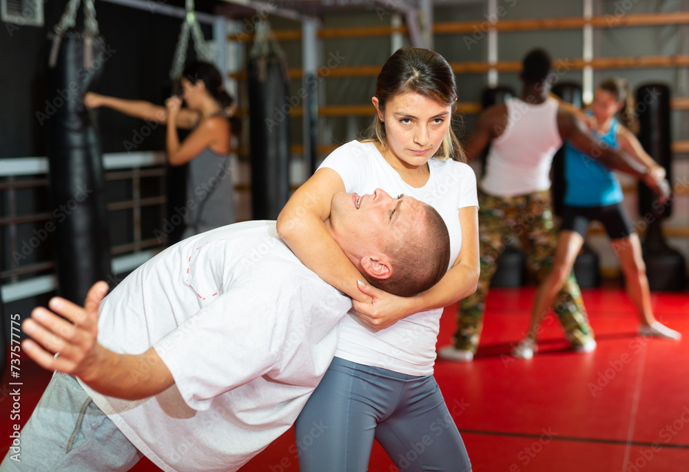 Latin woman practising neck grabbing with caucasian man during group self-defence training. African-american man exercising with woman in background.