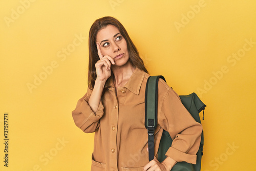 Middle aged woman prepped for hiking, yellow studio shot pointing temple with finger, thinking, focused on a task.