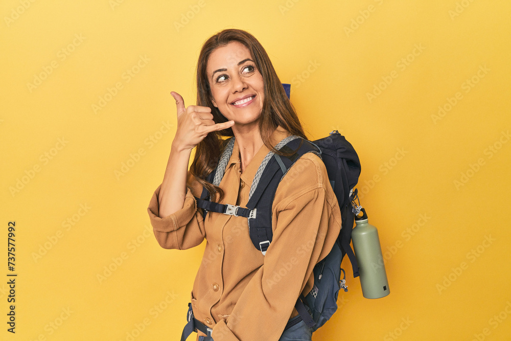 Middle aged woman prepped for hiking, yellow studio shot showing a mobile phone call gesture with fingers. Middle aged woman prepped for hiking, yellow studio shot showing a mobile phone call gesture with fingers.